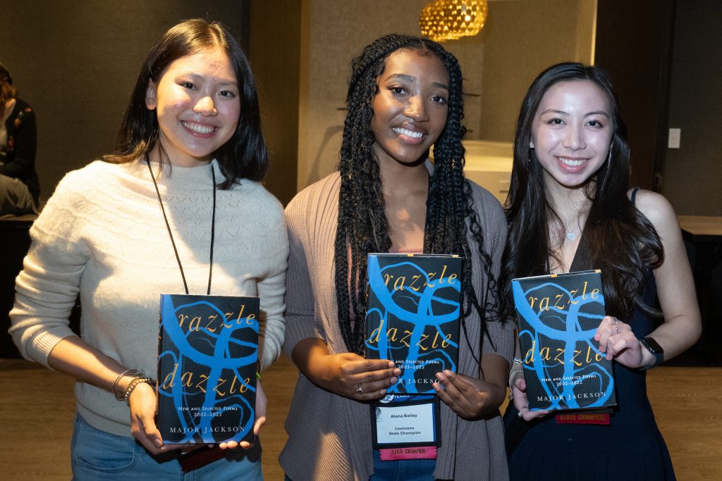 A group of three students hold books signed by a poet.